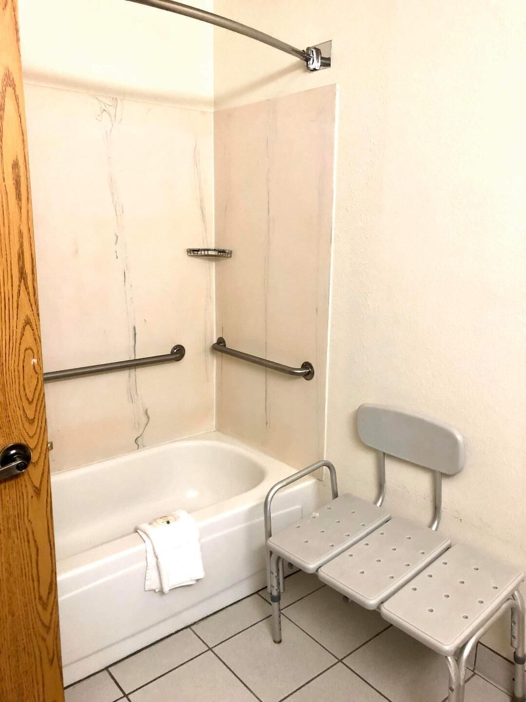 A bathroom with a bathtub, grab bars, a bench, and a towel.
