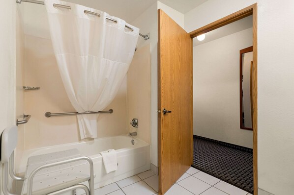 A bathroom with a bathtub, shower curtain, grab bars, and a wooden door.