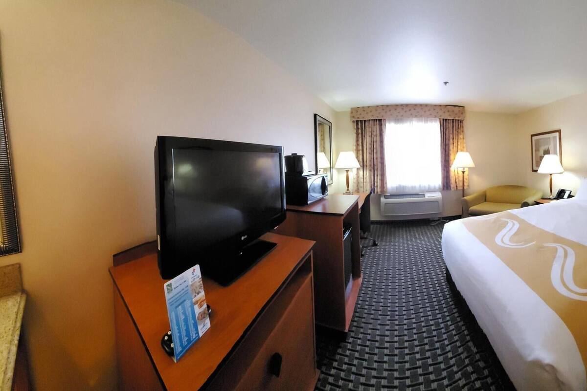 Ein Hotelzimmer mit Bett, Fernseher, Schreibtisch, Stuhl, Lampe und Fenster.