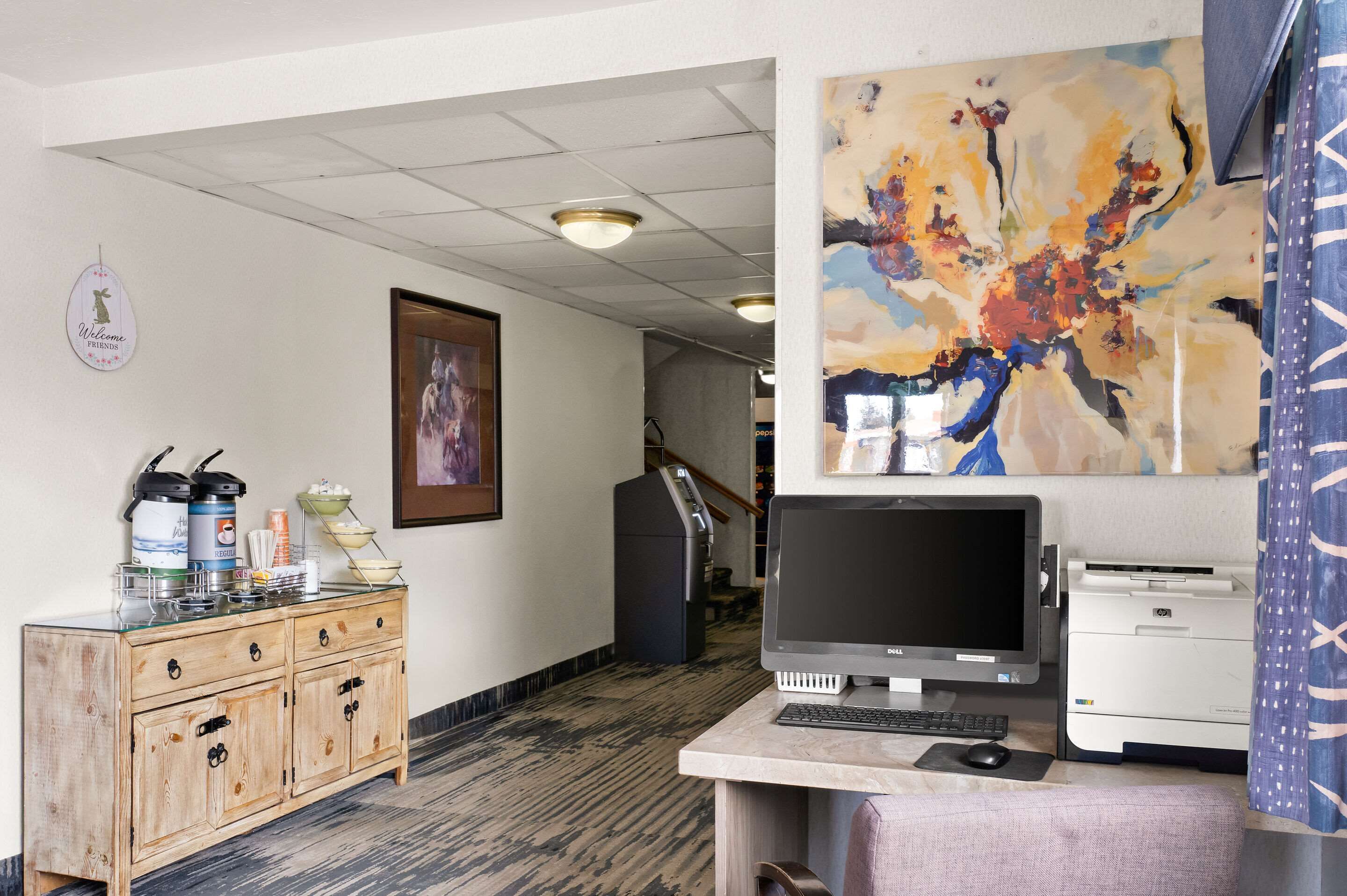 A reception area with a wooden desk, computer, printer, and a painting on the wall.