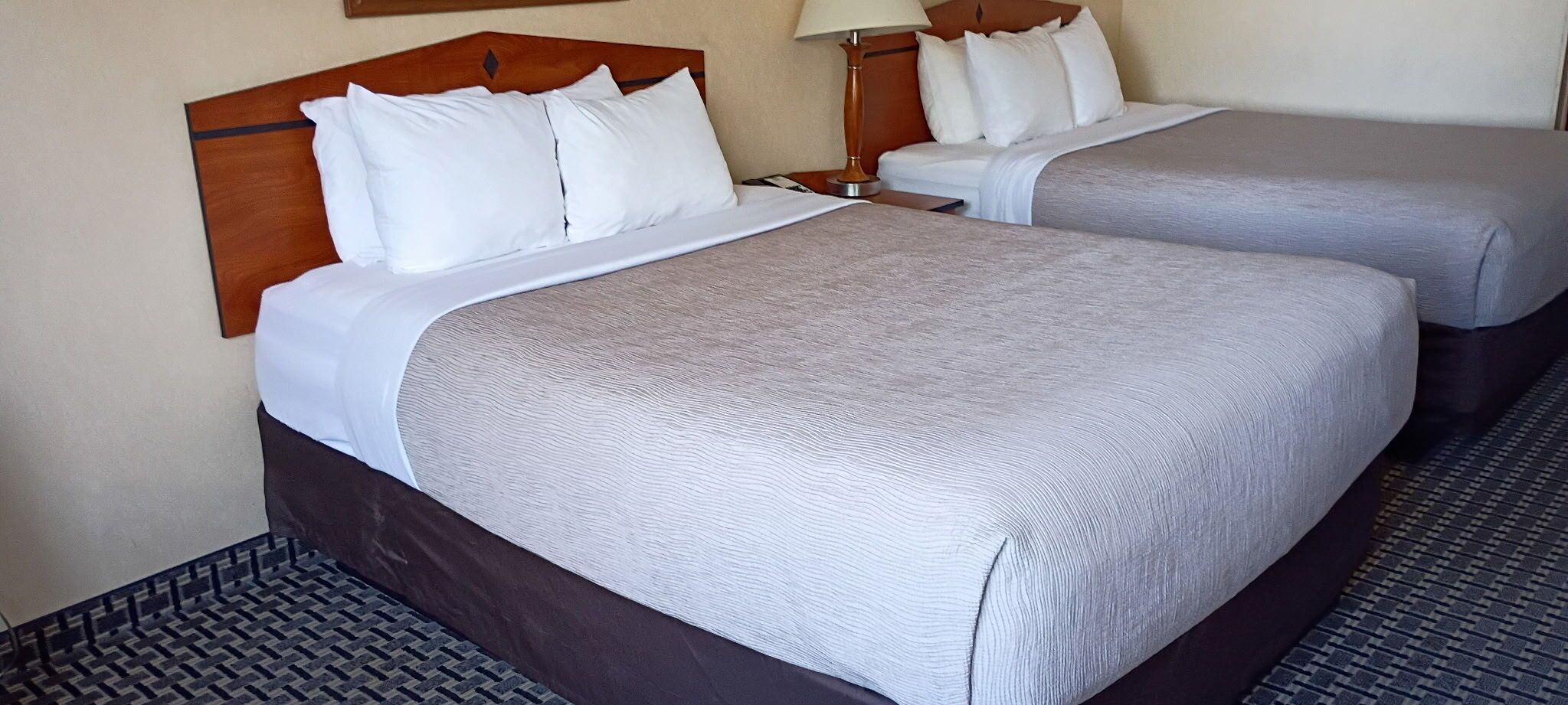 Two adjacent beds with wooden headboards, white bedding, and a patterned floor.