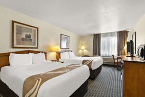 A hotel room with two beds, a desk, a chair, a television, and a window with curtains.
