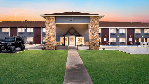 A building with a stone facade, numbered garage doors, and a paved driveway leading to a parking area. - Quality Inn Cheyenne I-25 South (Cheyenne)