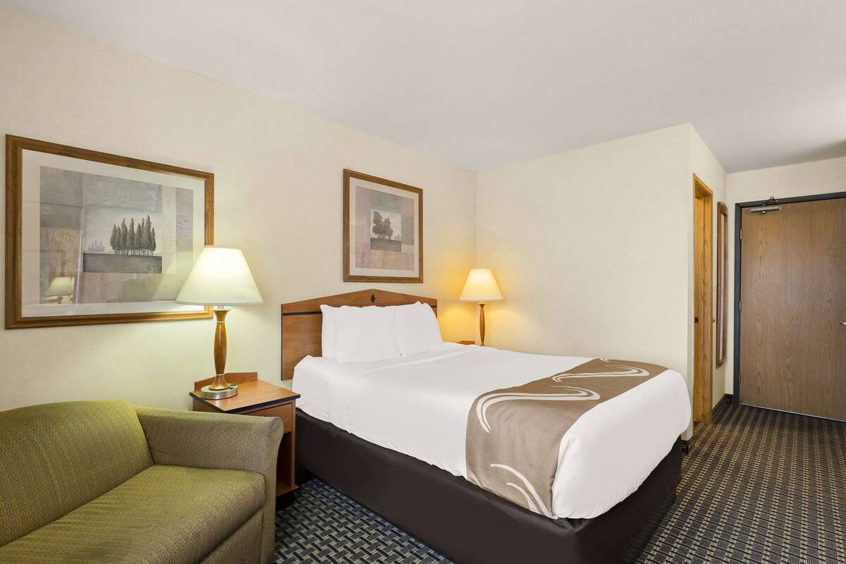 Ein Hotelzimmer mit einem Bett, zwei Nachttischlampen, einem grünen Sessel und zwei gerahmten Bildern an der Wand.