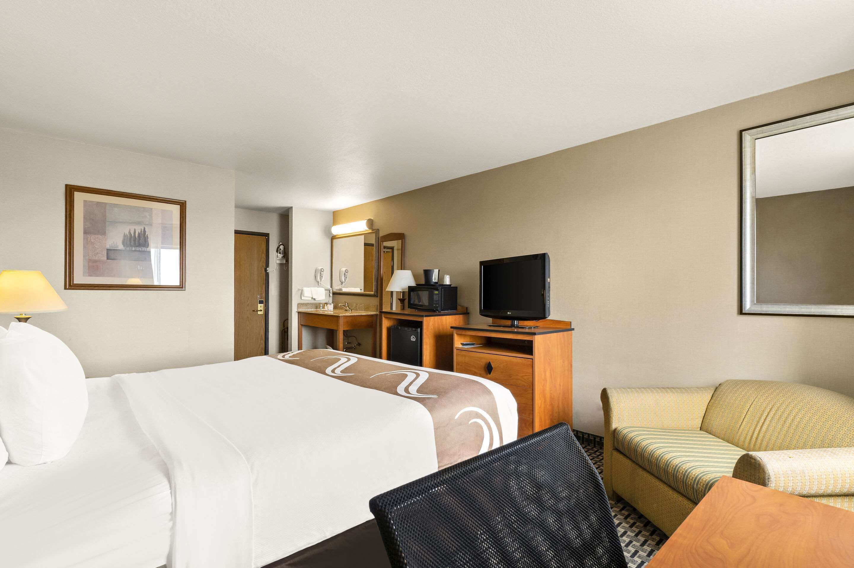 A hotel room with a bed, a desk with a computer, a television, a sofa, and a chair.
