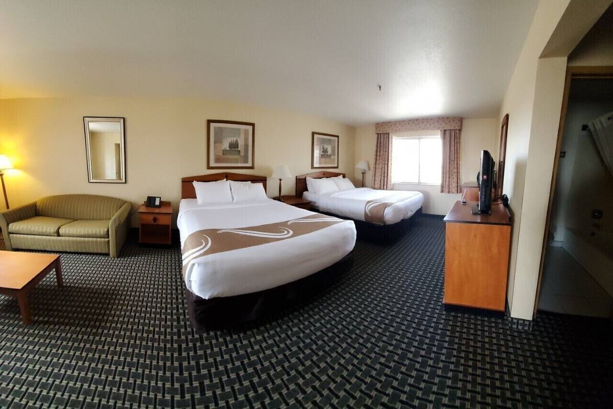 Ein Hotelzimmer mit zwei Betten, einem Sofa, einem Schreibtisch und einem Fernseher.