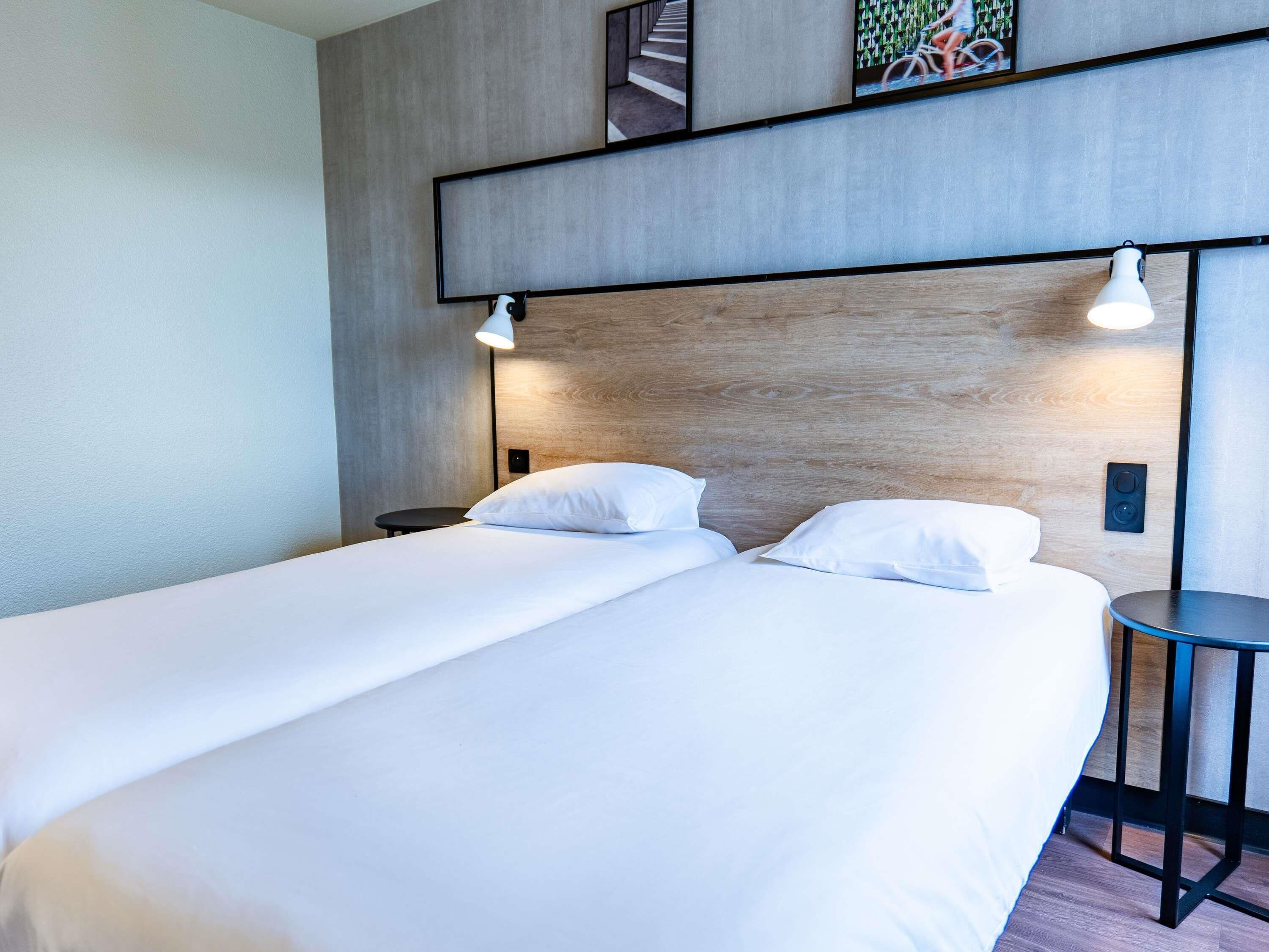 A hotel room with a double bed, a small table, and a wall-mounted shelf with a picture.