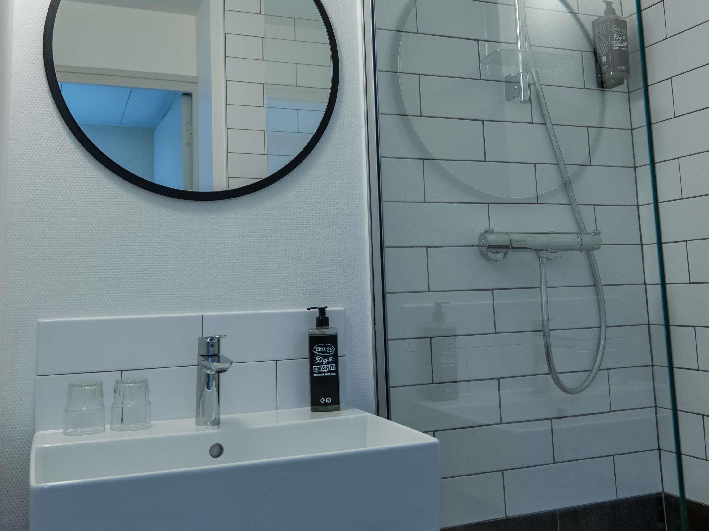 A bathroom with a white sink, a round mirror, and a glass shower enclosure.