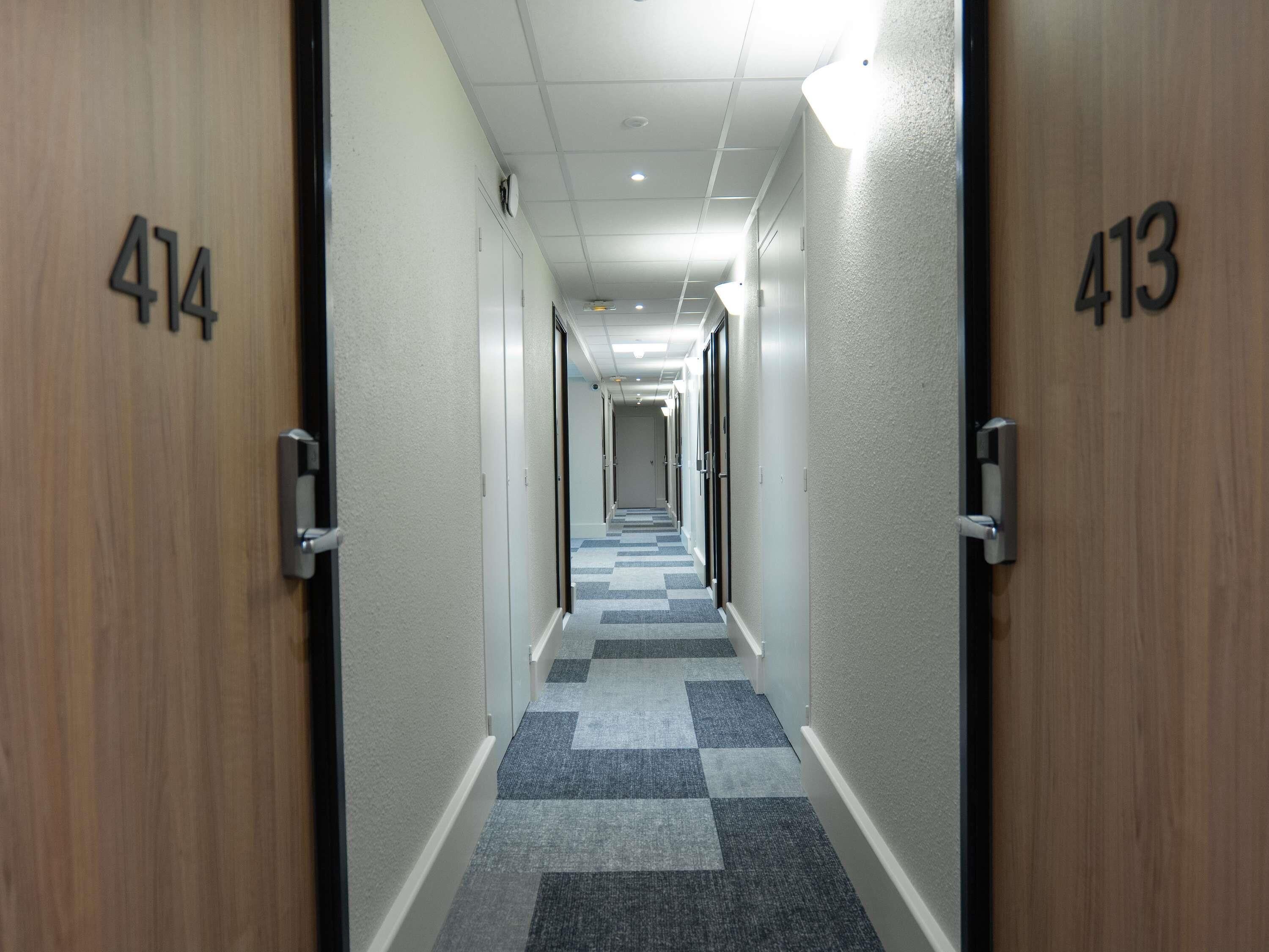 A hotel corridor with doors numbered 414 and 413, checkered carpet, and a ceiling with recessed lighting.