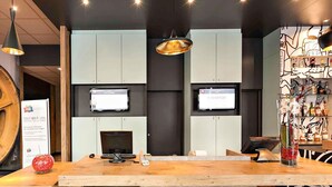 A reception desk with a wooden top, two monitors, a cash register, and a decorative vase. - ibis Agen Centre (Agen)