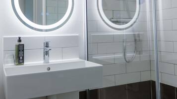 A modern bathroom with a white sink, two large mirrors, and a glass-enclosed shower.