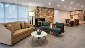 A modern living room with a stone fireplace, a sofa, a coffee table, and a dining area with chairs. - Fairfield Inn By Marriott Amesbury (Amesbury)