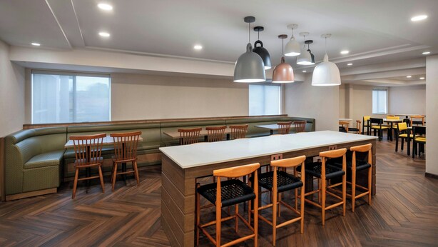 A spacious dining area with a long counter, multiple wooden chairs, and a green cushioned bench. - Fairfield Inn By Marriott Amesbury (Amesbury)