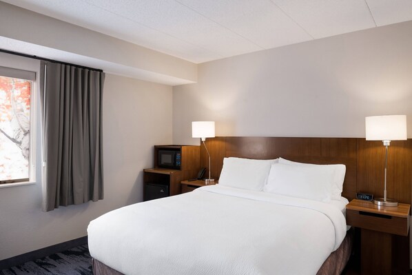Habitación de hotel con una cama grande, dos lámparas de noche, un televisor, un microondas y un escritorio pequeño con un teléfono.