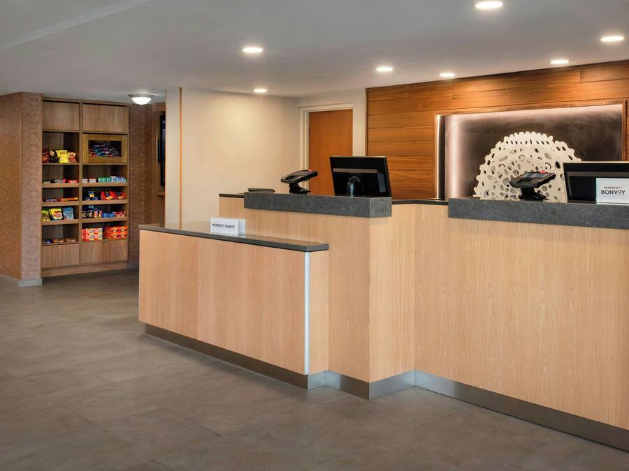 A hotel reception desk with a wooden finish, a digital screen, and a nameplate.