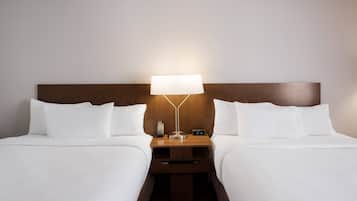 A hotel room with two beds, a nightstand with a lamp, and a digital clock.