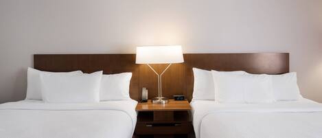 A hotel room with two beds, a nightstand with a lamp, and a digital clock.