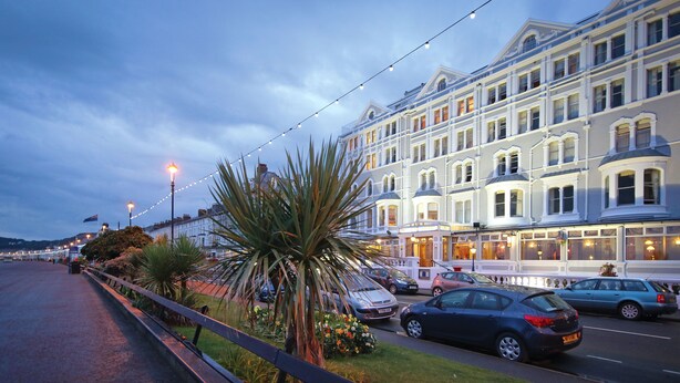 A row of white buildings with bay windows and a street with parked cars. - Imperial Hotel (Llandudno)