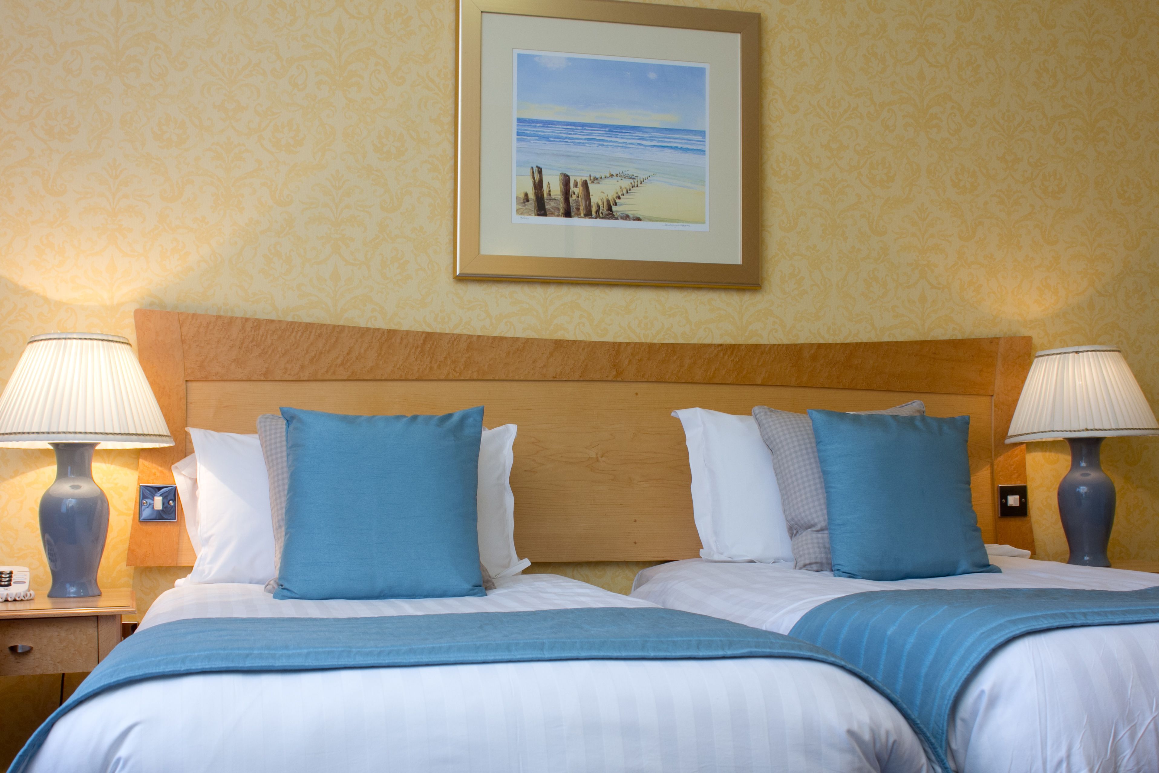 Habitación de hotel con dos camas, cabecero de madera y un cuadro enmarcado con una escena de playa en la pared.