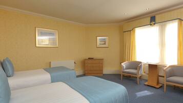 A hotel room with two beds, a wooden dresser, two armchairs, and two framed pictures on the wall.