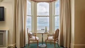 A room with a bay window, two chairs, a table with a bottle and glasses, and a television on the wall. - Imperial Hotel (Llandudno)
