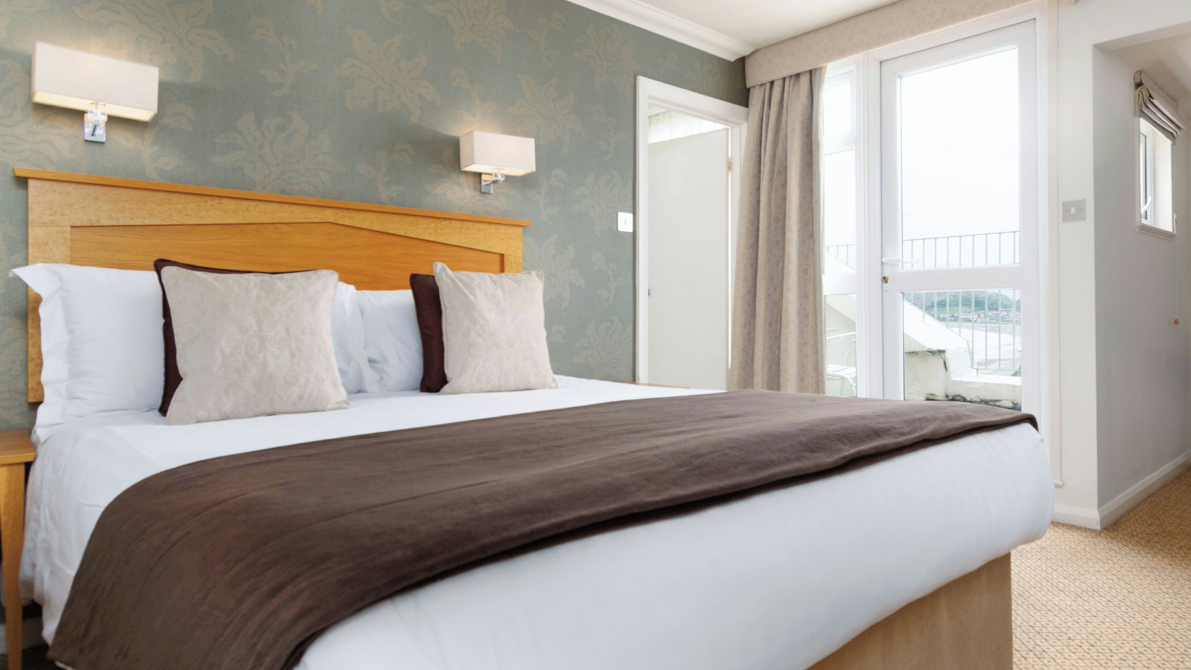 A hotel room with a large bed, a wooden headboard, two wall-mounted lights, and a view of the outside balcony.