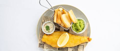 A plate with a fish and chips meal, including a side of mushy peas and tartar sauce.