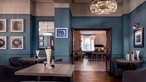 A hotel lobby with a wooden floor, blue walls, and framed artwork. There are tables and chairs for guests. - Imperial Hotel (Llandudno)