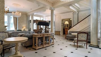 A grand lobby with a chandelier, a reception desk, a staircase, and a seating area with a table and sofas.