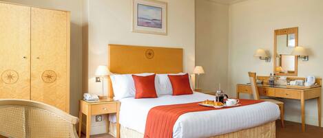 A hotel room with a large bed, a desk, a chair, a wardrobe, and a small table with a book.