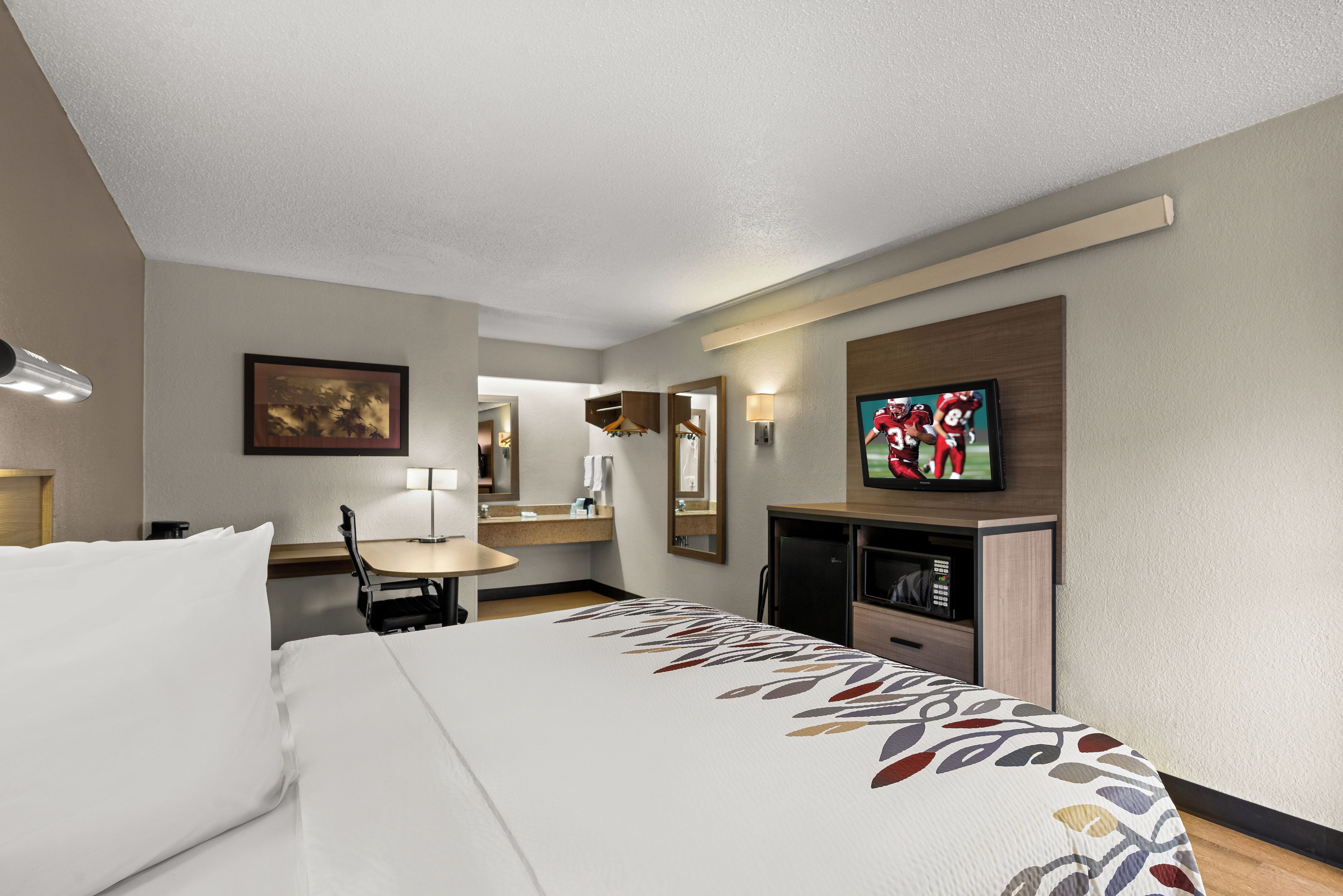 A hotel room with a bed, a desk, a television, and a mirror.