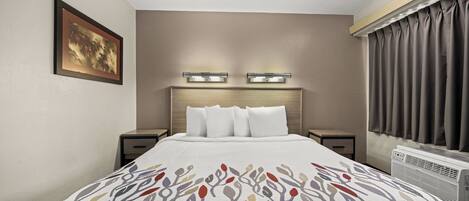 Habitación de hotel con una cama, mesitas de noche, lámpara de pared, ventana con cortinas e imagen enmarcada en la pared.