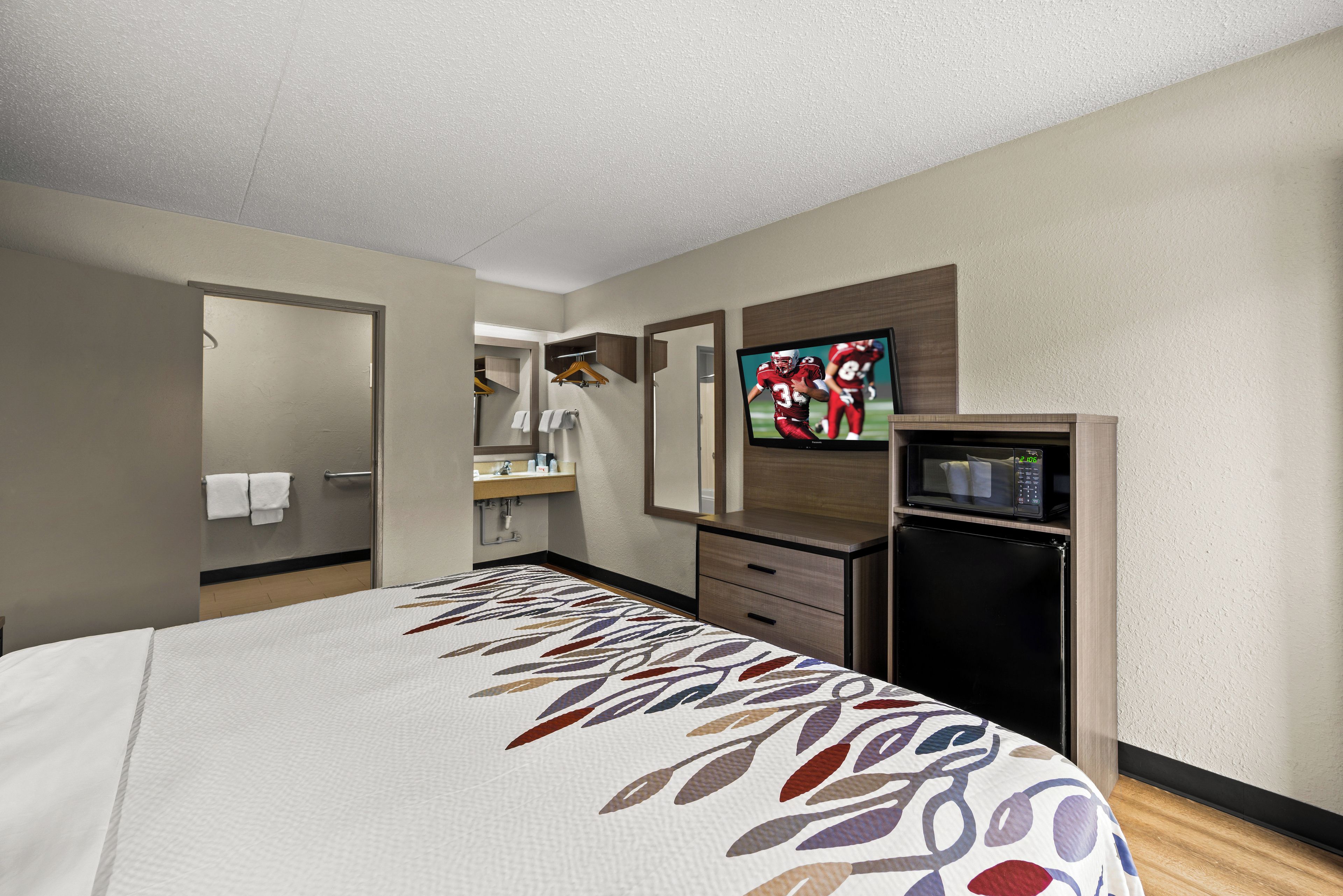 A hotel room with a bed, a television, a microwave, and a small kitchenette.