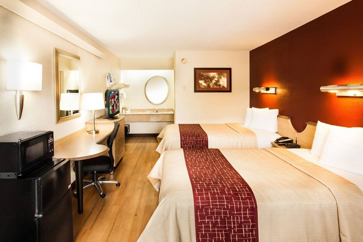 A hotel room with two beds, a desk with a TV, a mirror, a painting, and a clock on the wall.