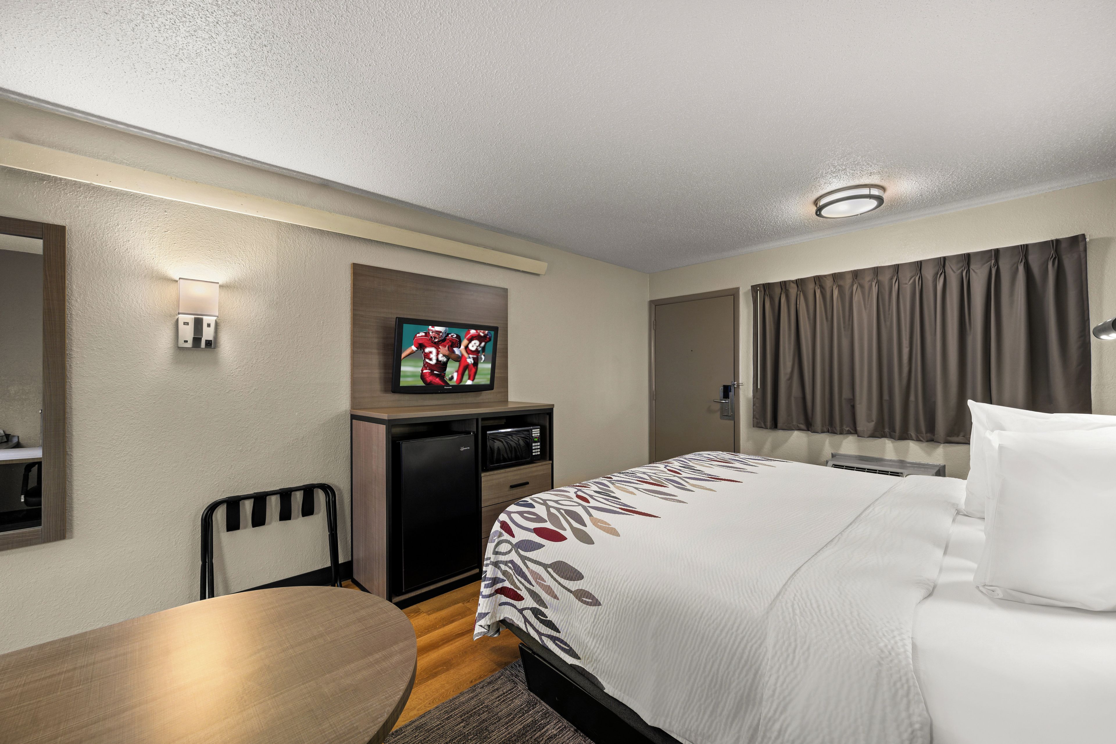 Habitación de hotel con una cama, un escritorio, un televisor y un microondas.
