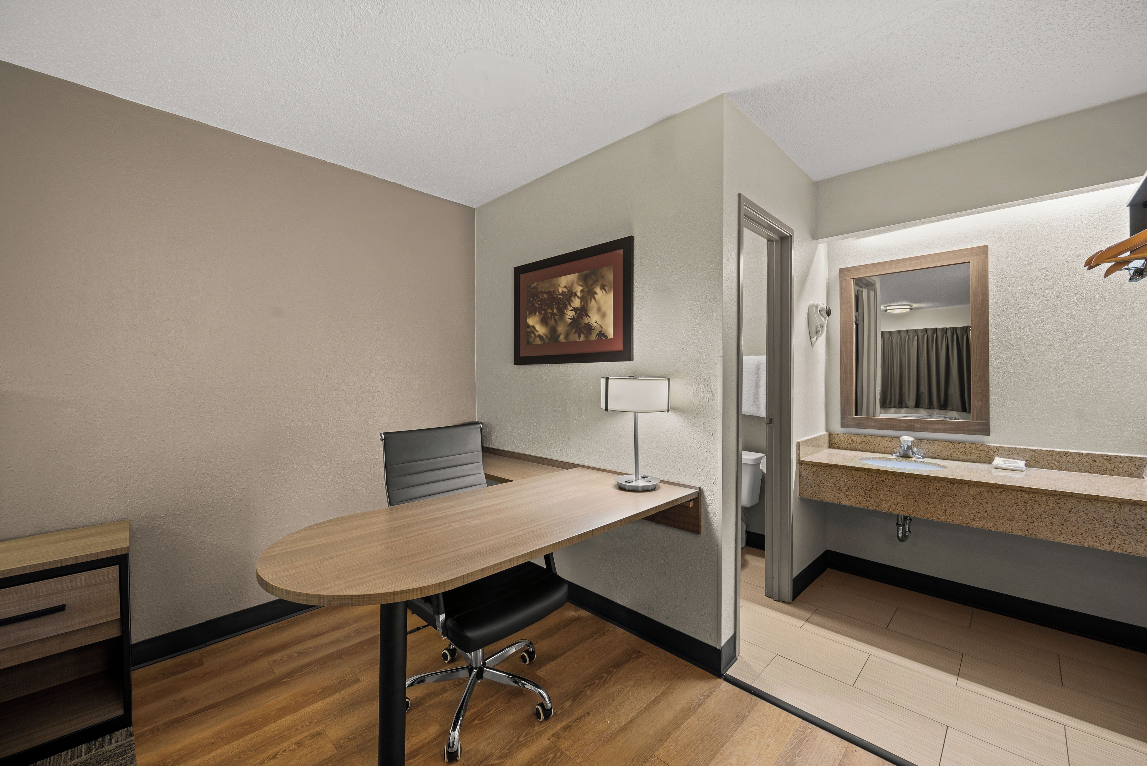 A hotel room with a desk, chair, and a bathroom with a sink and mirror.