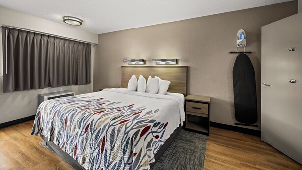 A hotel room with a bed, a nightstand, a dresser, a large mirror, and a door. - Red Roof Inn Detroit - Royal Oak/ Madison Heights (Madison Heights)