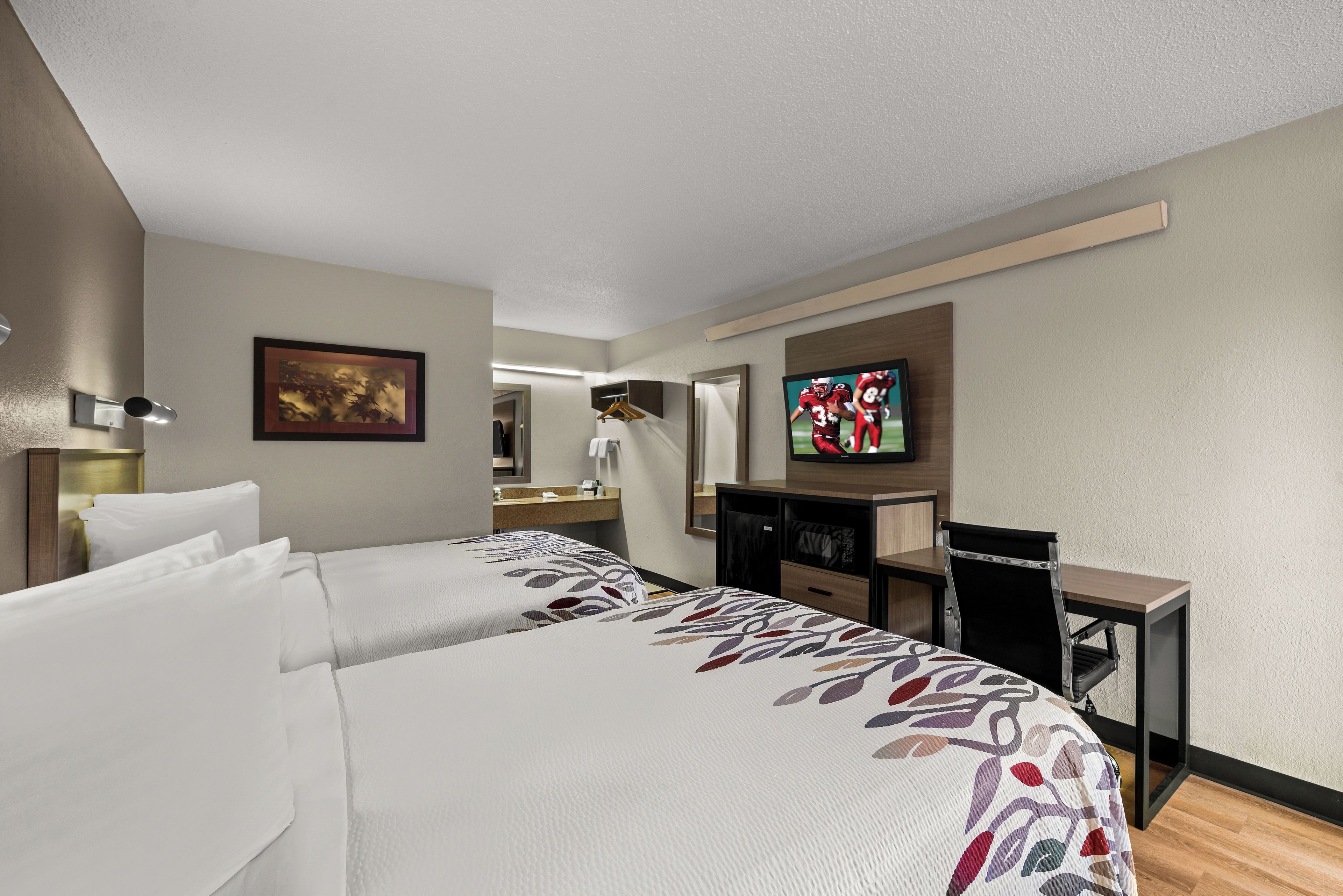 Una habitación de hotel con dos camas, un escritorio, un televisor y un espejo.