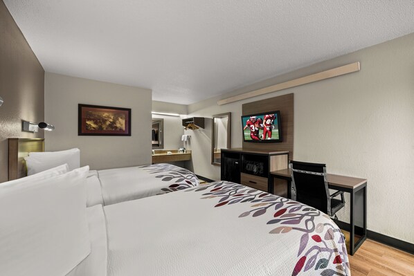 A hotel room with two beds, a desk, a television, and a mirror. - Red Roof Inn Detroit - Royal Oak/ Madison Heights (Madison Heights)