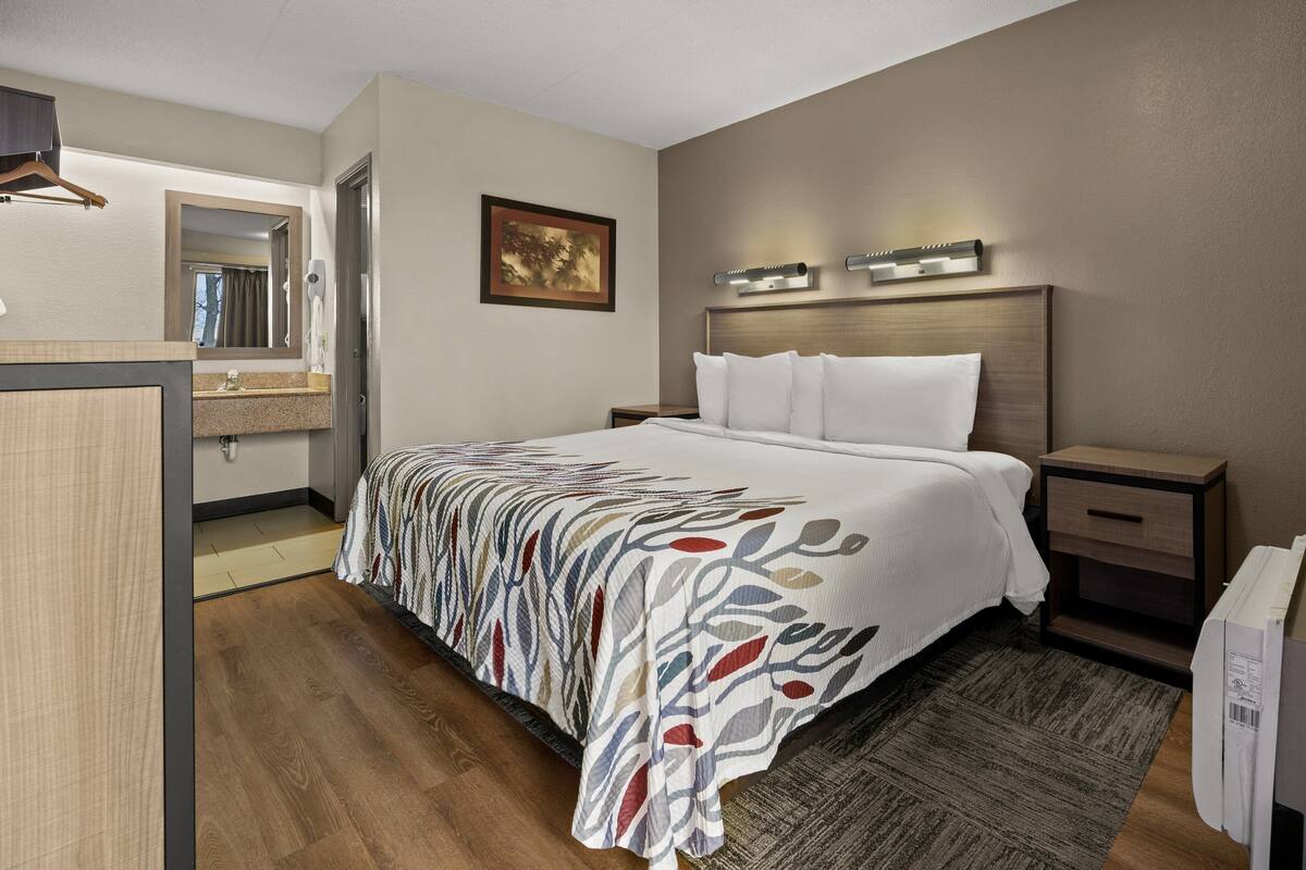 A hotel room with a bed, bedside tables, a mirror, and a painting on the wall.