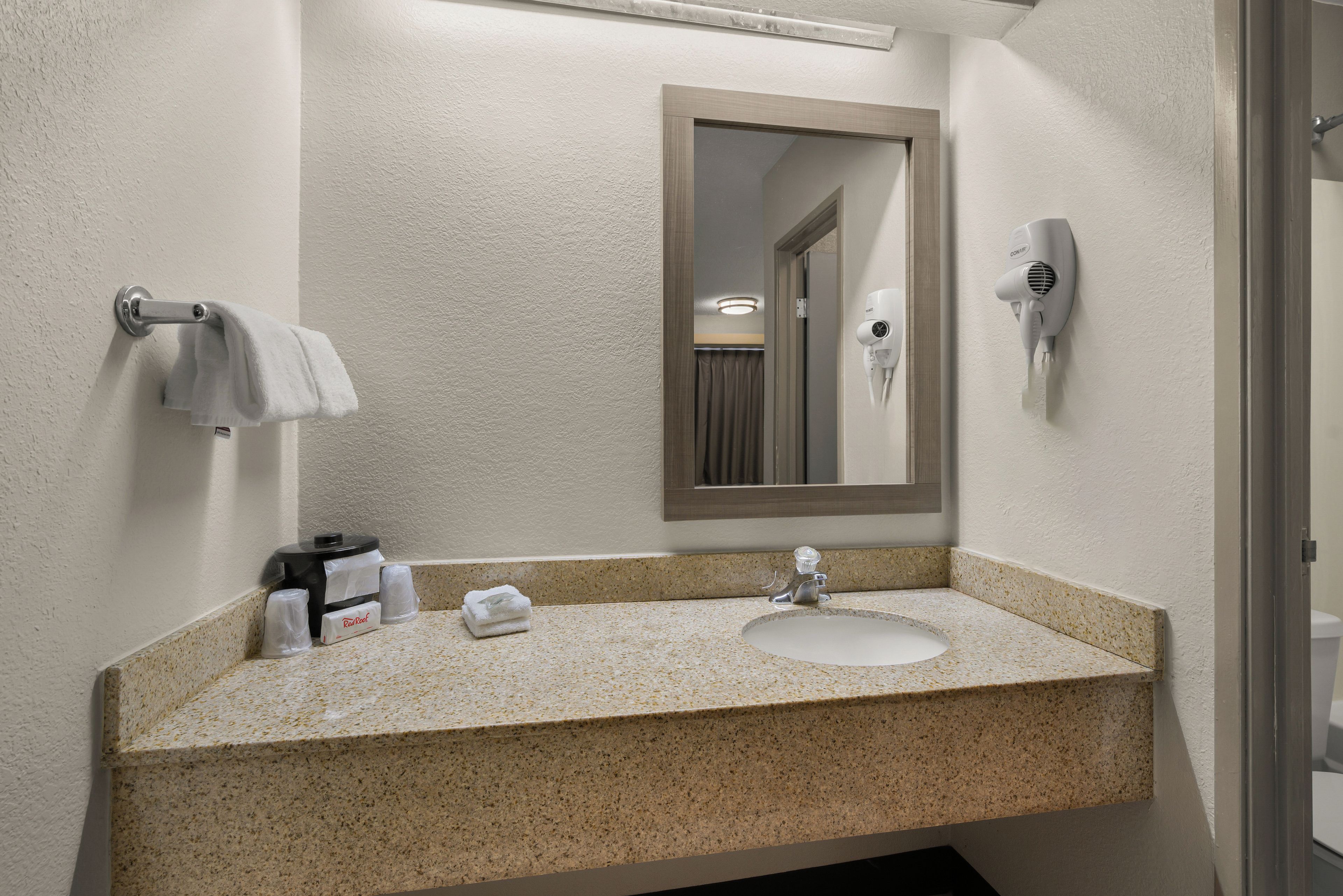 Un baño con encimera de granito, lavabo, toallero, secador de pelo y espejo.