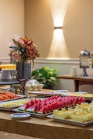 Un tavolo per buffet con diversi tipi di frutta e un centro tavola floreale.