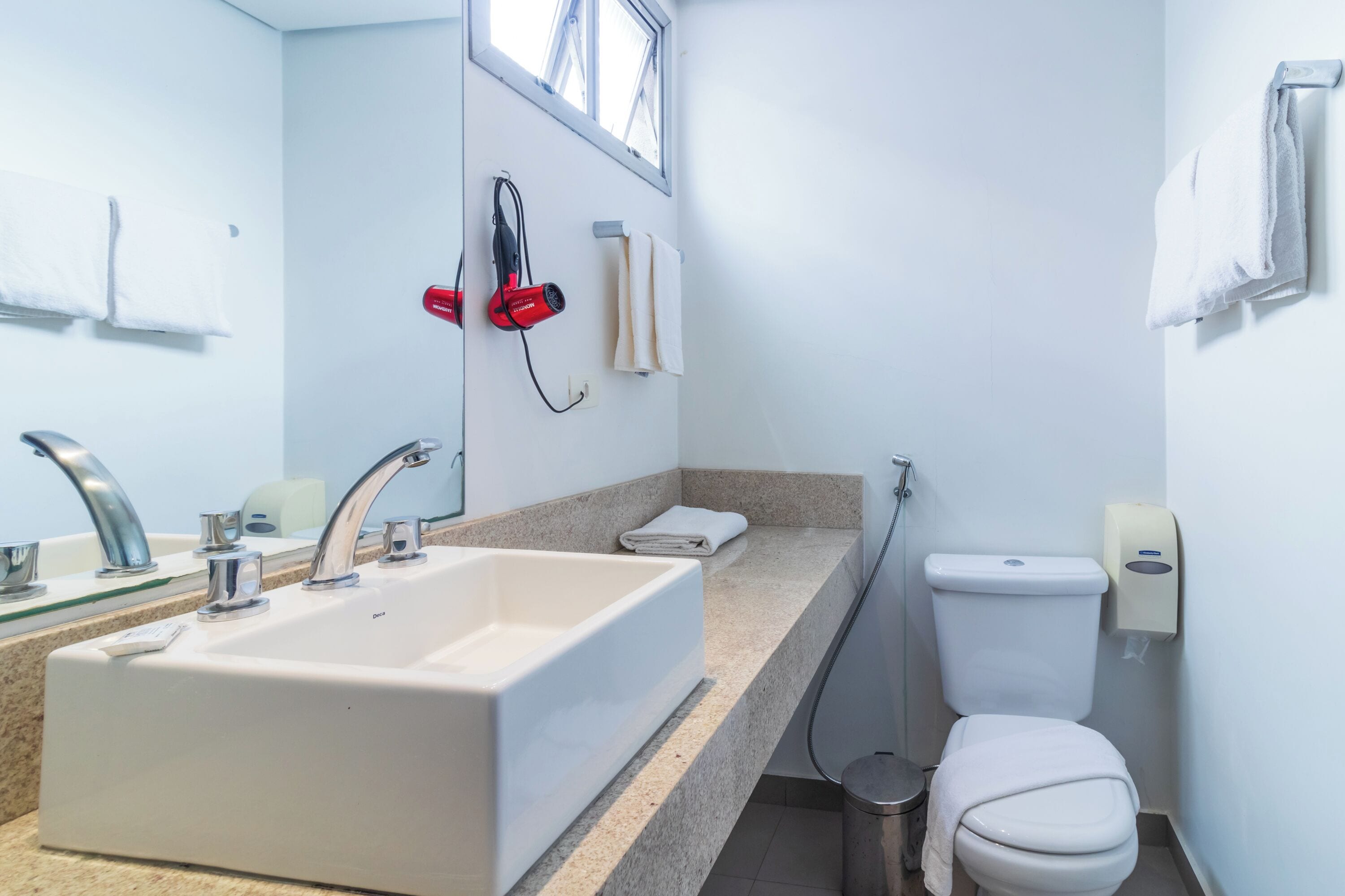 Un baño con lavamanos, espejo, toallero y retrete.