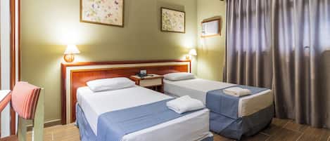 A hotel room with two beds, a wooden headboard, a desk with a lamp, and a window with curtains.