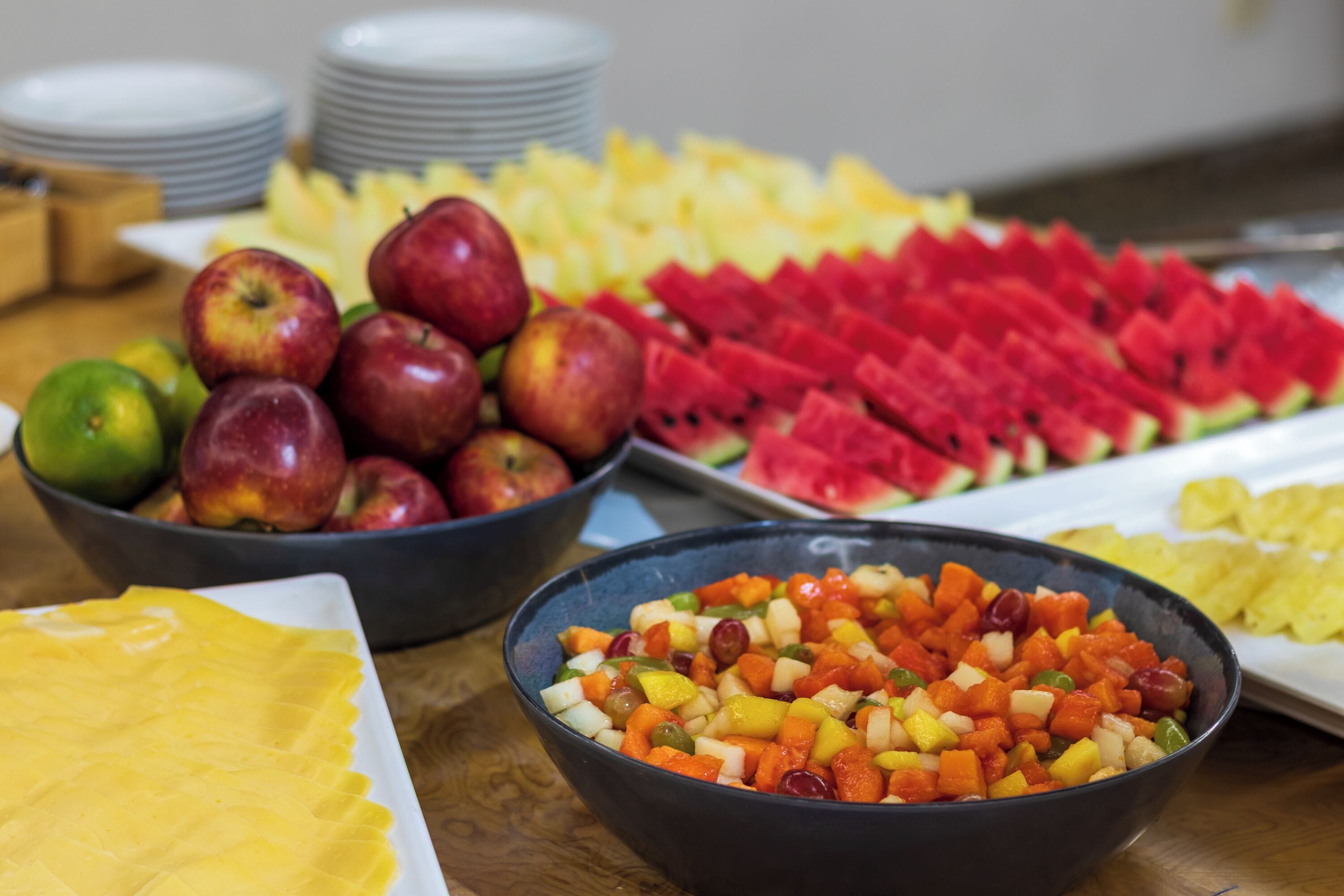 A table with various fruits including apples, watermelon, and a bowl of mixed fruit salad.