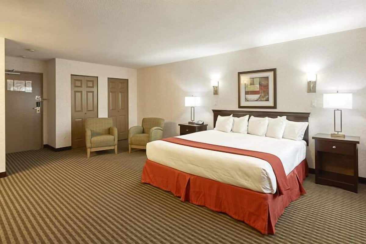 A hotel room with a large bed, two chairs, a desk, and a door.