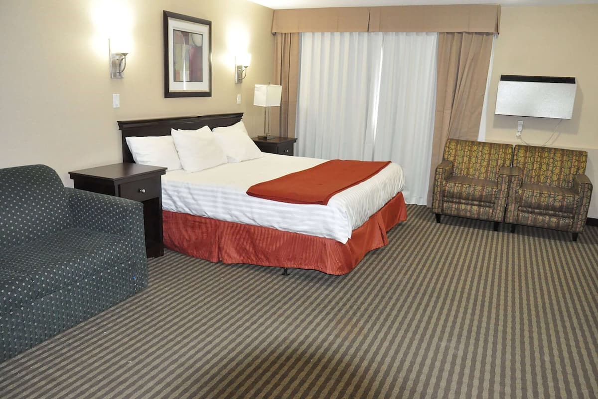 A hotel room with a large bed, a sofa, a chair, a TV, and a lamp.