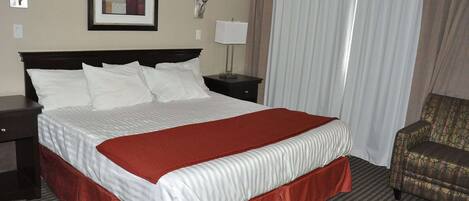 Habitación de hotel con una cama grande, una silla, una mesita de noche, una lámpara y un cuadro enmarcado en la pared.