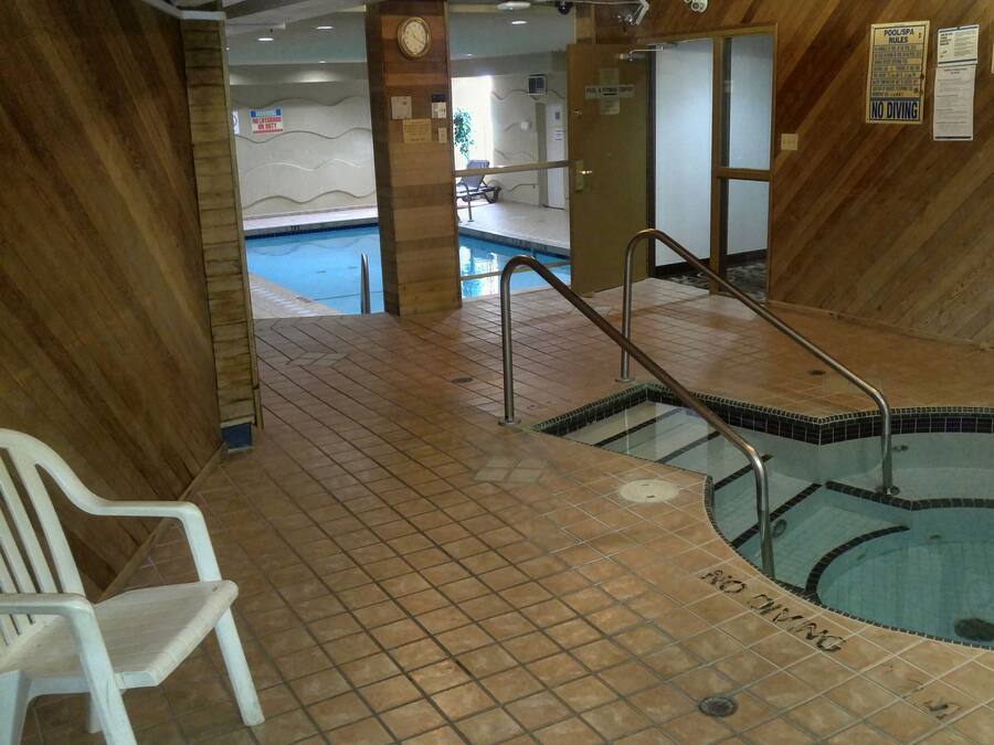 Zona de piscina con suelo de baldosas, una silla blanca y varias señales, incluyendo 'NO DIVING'.