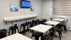 A modern conference room with white tables and black chairs, a flat-screen TV mounted on the wall, and abstract art pieces. - Econo Lodge Motel Village (Calgary)